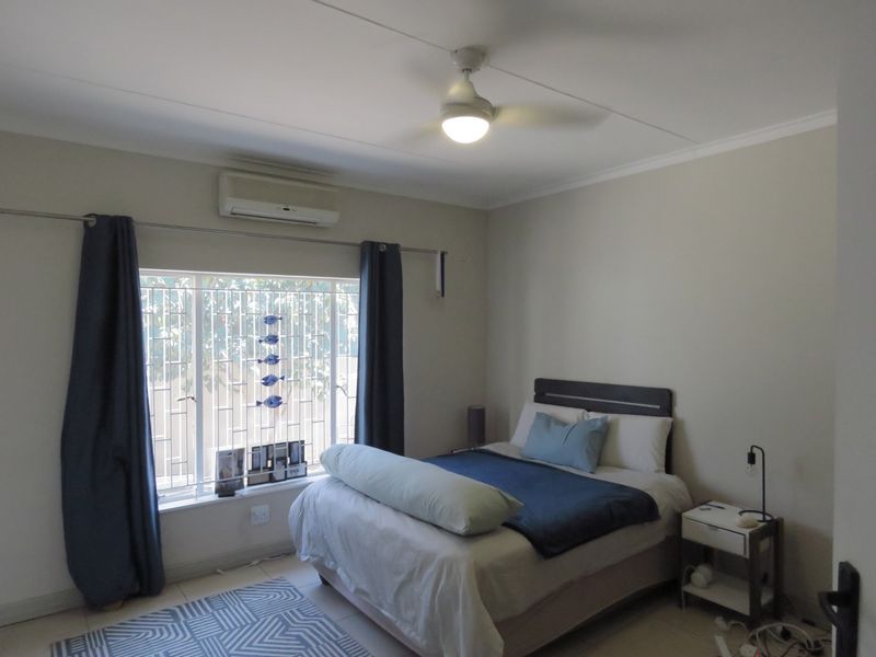 A functional bedroom featuring tiled flooring, a ceiling fan, and a wall-mounted split-system air conditioner for climate control.