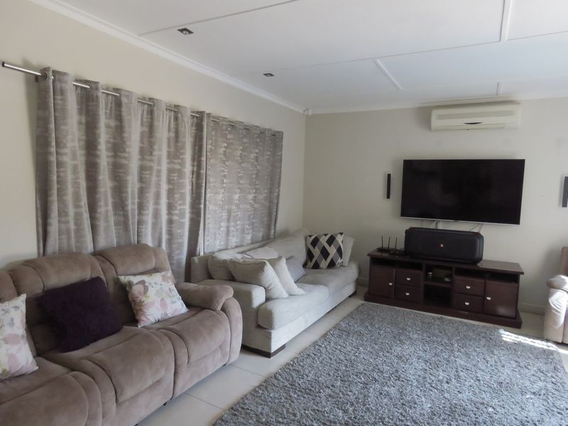 A comfortable living room featuring a wall-mounted air conditioning unit, recessed ceiling lighting, and neutral wall finishes.