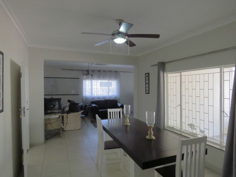 Open plan living and dining area featuring tiled flooring, ceiling fan, and large windows with security bars.