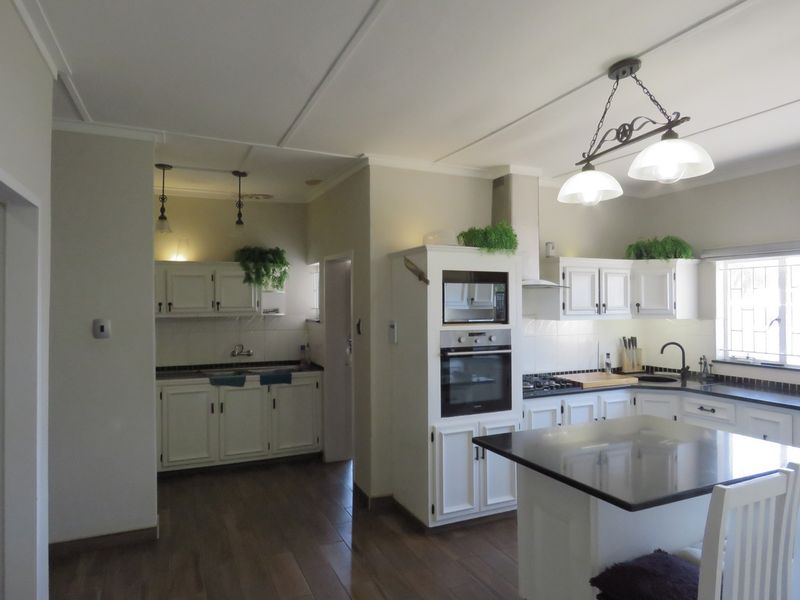 A well-appointed kitchen featuring white cabinetry, granite countertops, a central island, and integrated appliances including an oven, microwave, and gas hob.