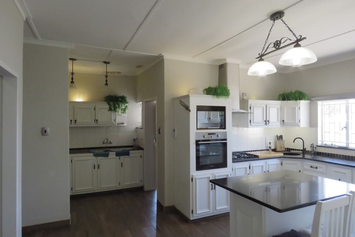 A well-appointed kitchen featuring white cabinetry, granite countertops, a central island, and integrated appliances including an oven, microwave, and gas hob.