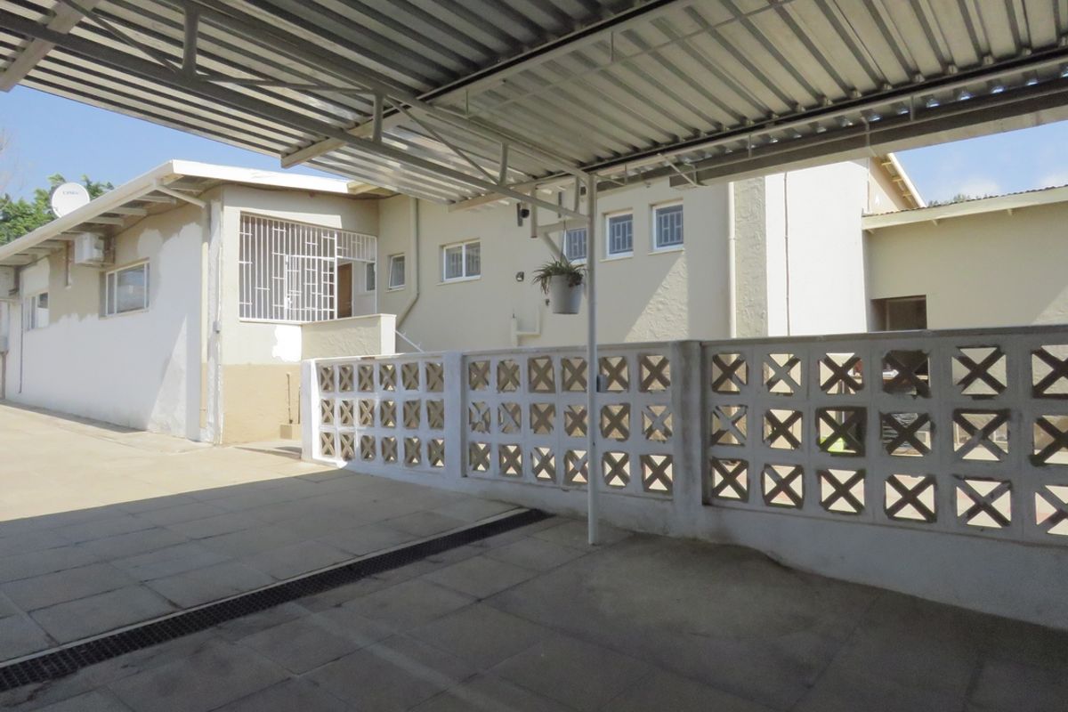 A covered patio area featuring a corrugated metal roof, paved flooring, and a decorative breeze block wall overlooking the rear exterior of the house.