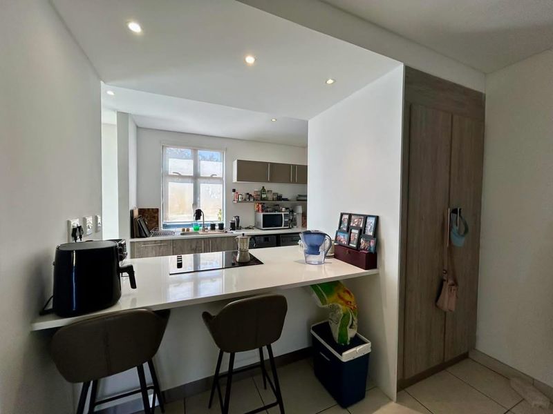 Modern kitchen featuring a breakfast bar with integrated hob, ample built-in cabinetry, quartz countertops, and recessed lighting, creating a functional and open cooking space.