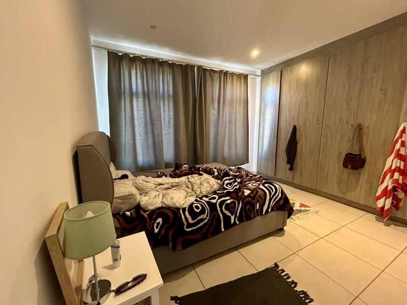 A well-proportioned bedroom featuring neutral tiled flooring, extensive built-in wooden cabinetry, and large windows dressed with floor-to-ceiling curtains.