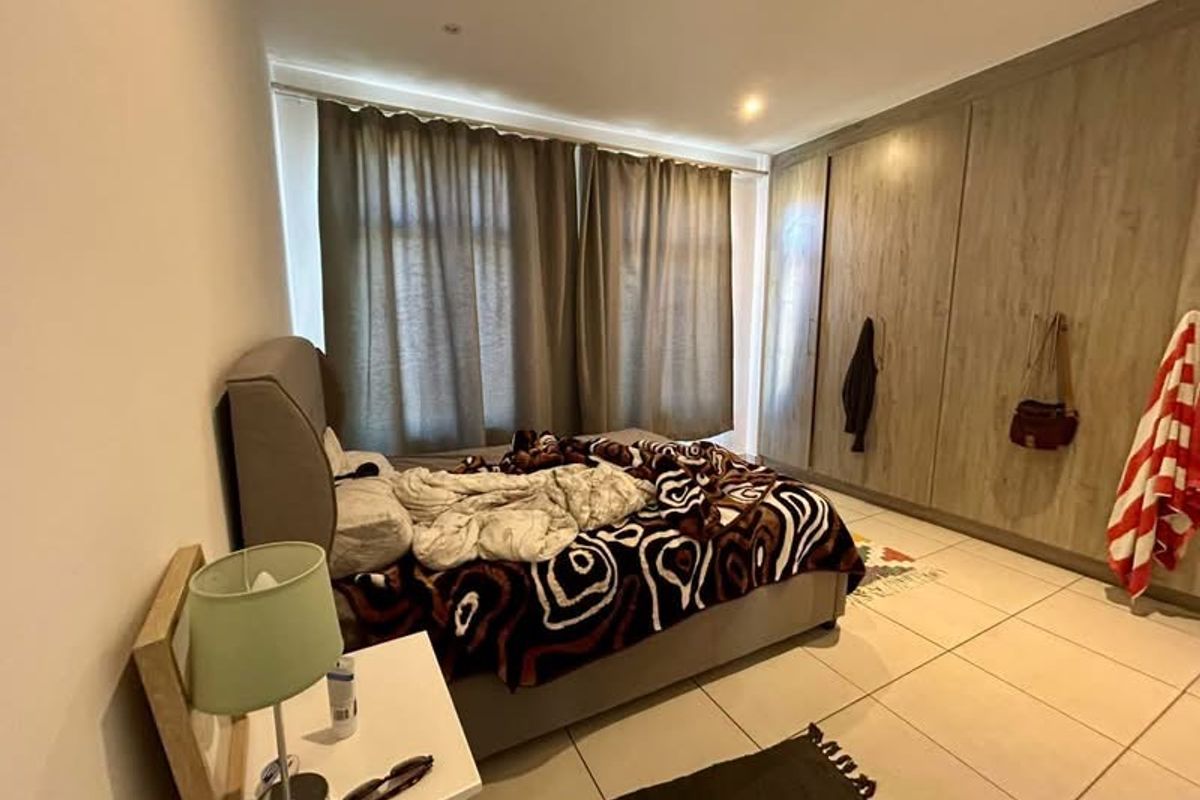 A well-proportioned bedroom featuring neutral tiled flooring, extensive built-in wooden cabinetry, and large windows dressed with floor-to-ceiling curtains.