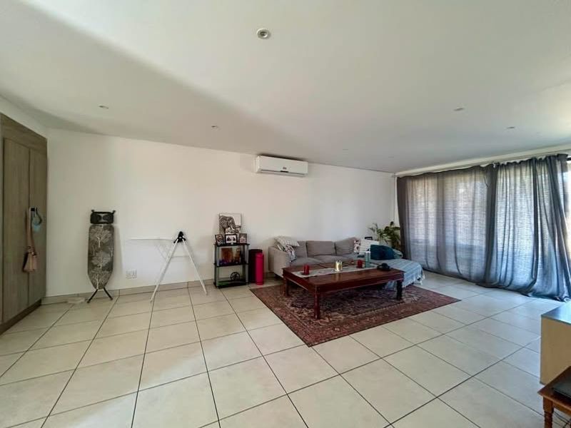 Spacious living room featuring neutral tiled flooring, recessed lighting, a wall-mounted air conditioning unit, and a built-in storage cupboard.