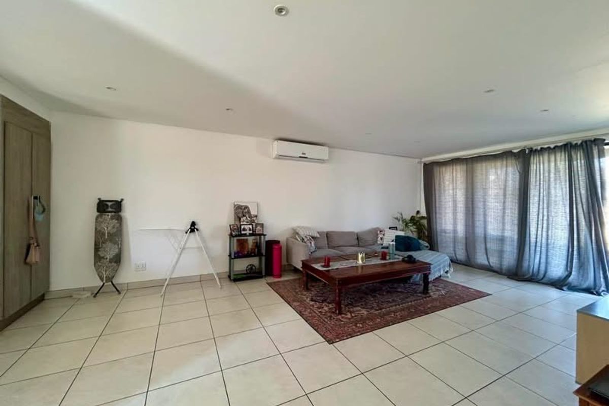 Spacious living room featuring neutral tiled flooring, recessed lighting, a wall-mounted air conditioning unit, and a built-in storage cupboard.
