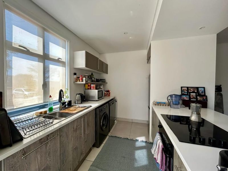 Modern kitchen featuring sleek wood-grain cabinetry, stone countertops, integrated induction hob, and built-in oven, with ample natural light from a large window.