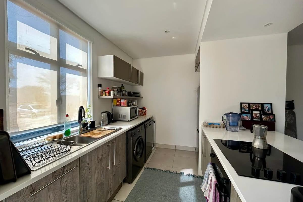 Modern kitchen featuring sleek wood-grain cabinetry, stone countertops, integrated induction hob, and built-in oven, with ample natural light from a large window.