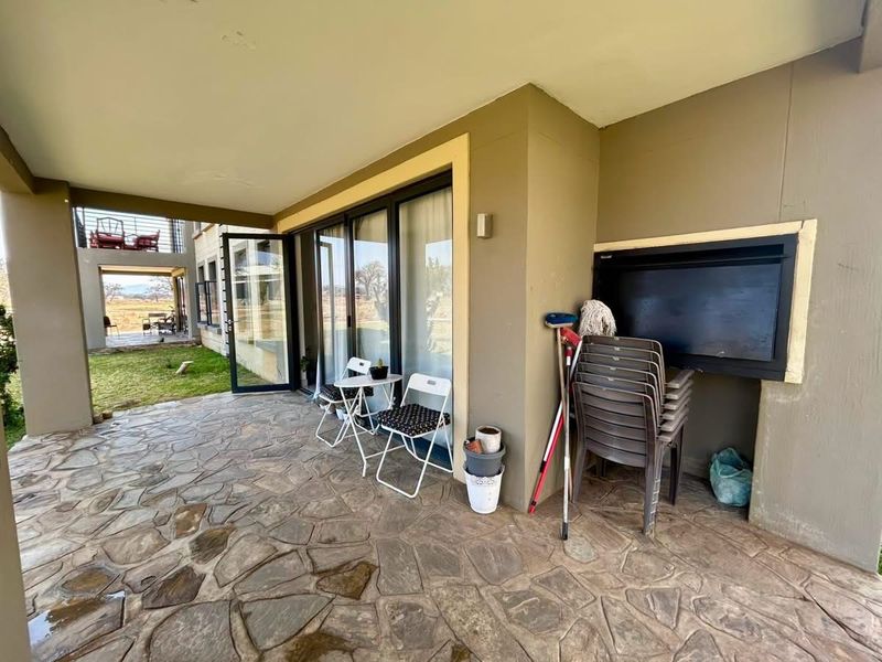 A covered patio area featuring stone paving and a built-in braai, providing direct access to the garden through sliding glass doors.