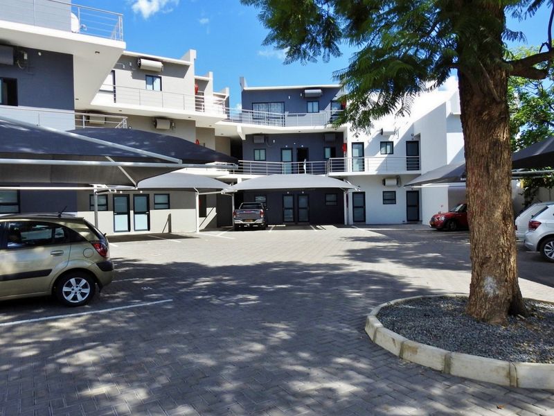Exterior view of a modern apartment complex featuring paved parking areas, shade cloth carports, and multi-level balconies with external access.