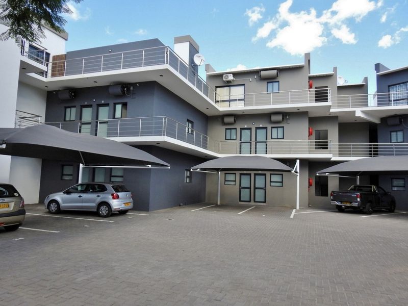 Modern apartment complex exterior featuring paved parking area, shade cloth carports, and multi-level balconies with stainless steel railings.