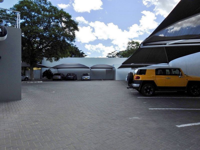 A paved outdoor parking area featuring multiple shade cloth carports and secure boundary walls.