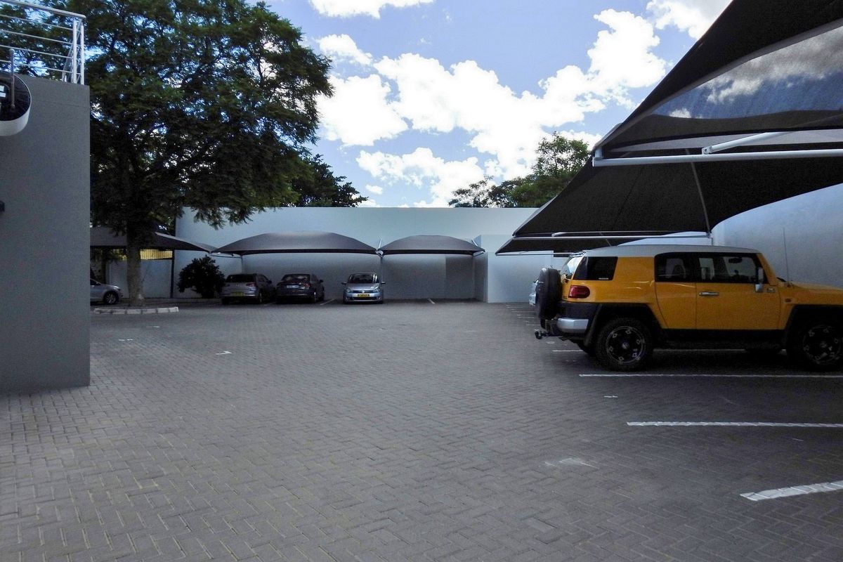 A paved outdoor parking area featuring multiple shade cloth carports and secure boundary walls.
