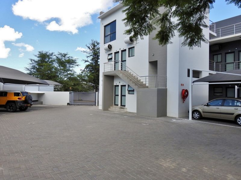 Front view of a modern apartment complex featuring paved parking, covered carports, and external stair access to upper units.