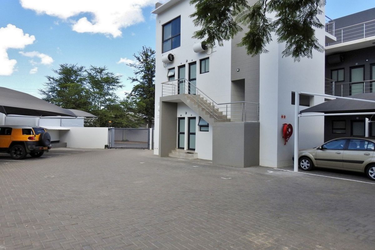 Front view of a modern apartment complex featuring paved parking, covered carports, and external stair access to upper units.