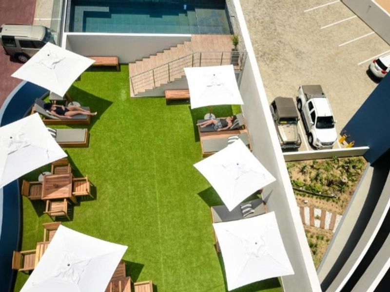An elevated aerial view of a communal pool area featuring a swimming pool, artificial lawn, and paved access stairs.