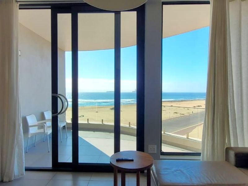 Modern living room featuring large sliding glass doors that open onto a balcony with expansive ocean and beach views.