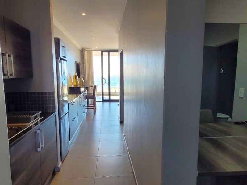 An open-plan apartment layout featuring a modern kitchen with dark cabinetry, tiled flooring, and a seamless transition to a balcony with ocean views.