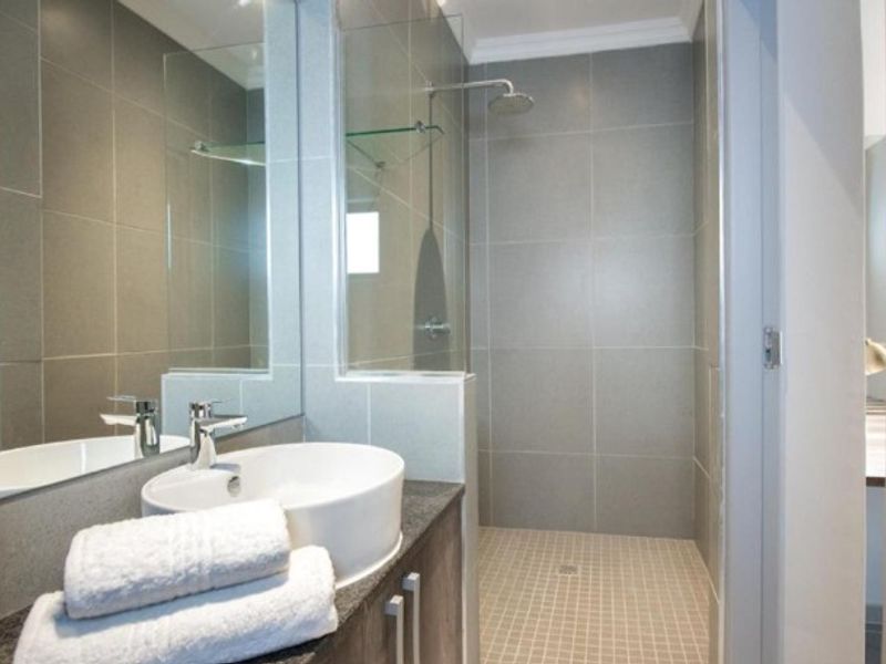 Modern bathroom featuring a vessel sink on a stone vanity, a spacious walk-in shower with a glass screen, and neutral grey wall tiling.