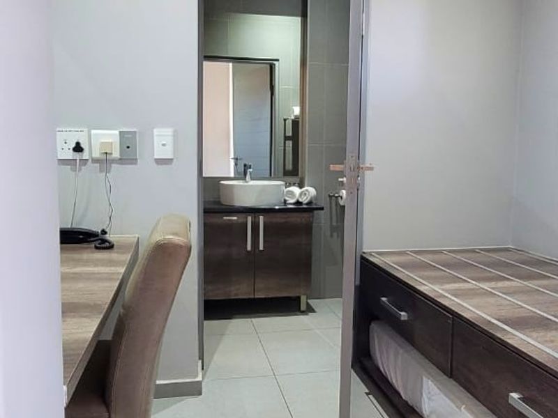 A modern bedroom featuring tiled flooring, a built-in desk, and an en-suite bathroom with a vanity basin and contemporary cabinetry.