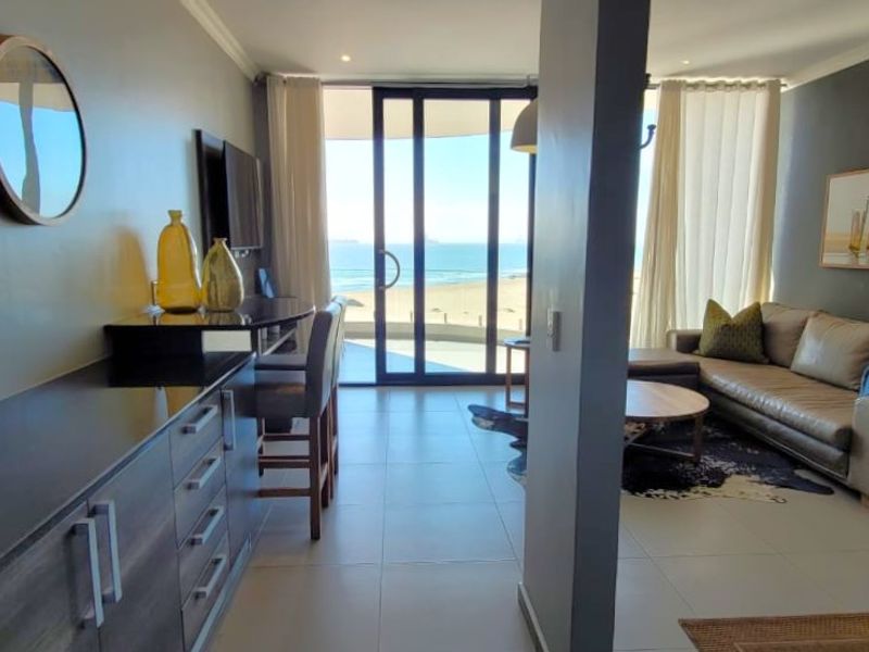 Open-plan living area featuring modern cabinetry, tiled floors, and large sliding glass doors opening to a scenic beach view.