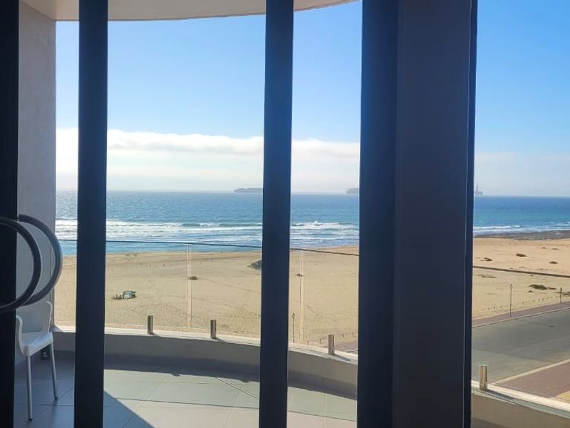A scenic view of the ocean and beach from a balcony featuring a modern glass balustrade.