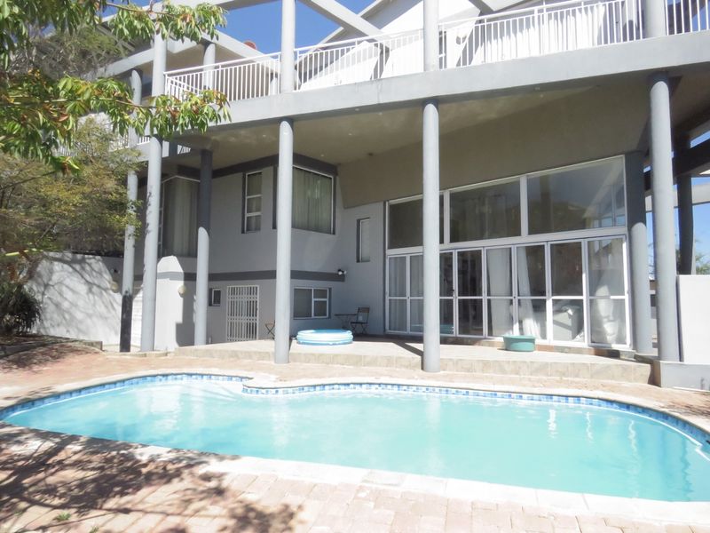 Rear exterior view featuring a swimming pool, paved surround, and a multi-level patio area with structural columns and large sliding glass doors.
