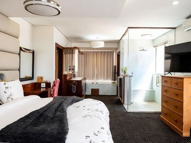 Spacious bedroom featuring an integrated en-suite bathroom with a glass-enclosed shower, built-in bathtub, and vanity, complemented by modern lighting and air conditioning.