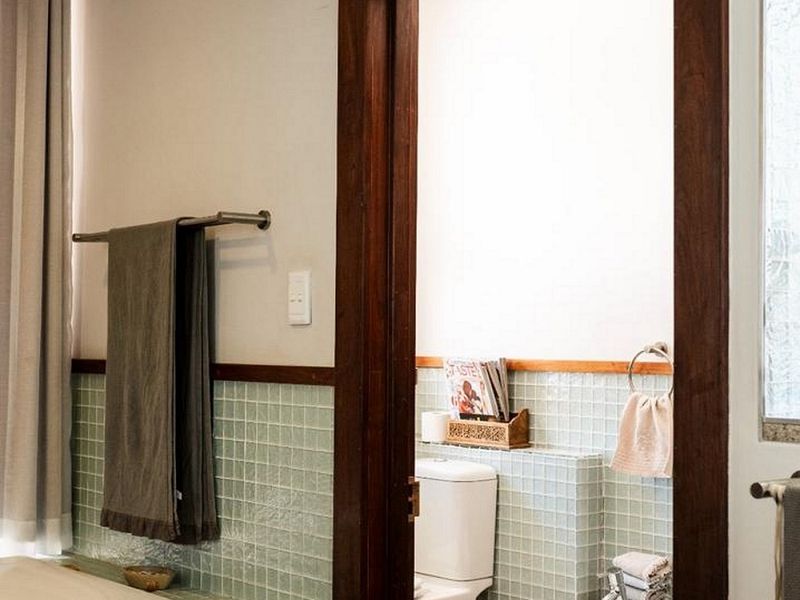 A bathroom featuring a built-in bathtub with light green mosaic tiling, a separate toilet and bidet area, and classic timber door framing.