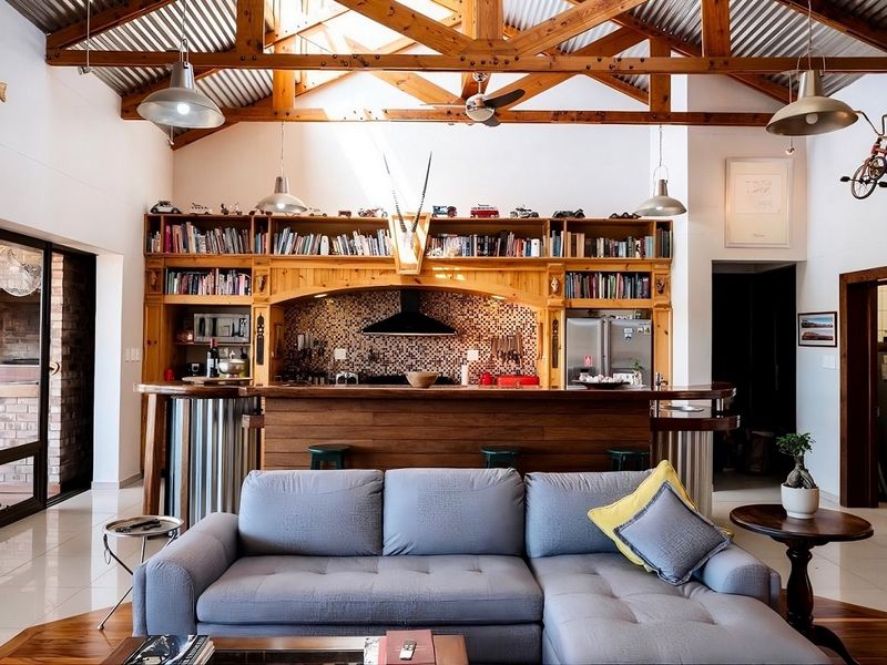 Spacious open-plan living area featuring exposed timber roof trusses, a large built-in wooden kitchen unit with mosaic backsplash, and seamless indoor-outdoor flow.
