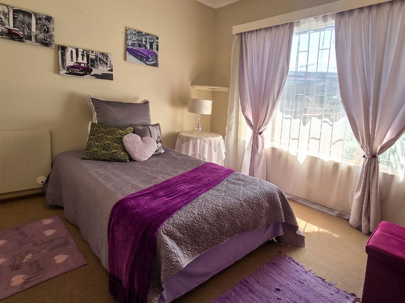 A cozy bedroom featuring carpeted flooring, a wall-mounted heater, and a window fitted with security bars.