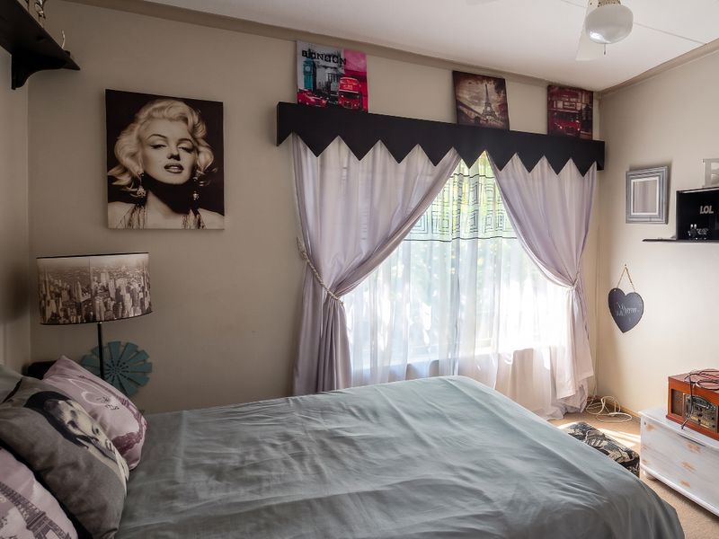 A bedroom featuring a ceiling fan and a window with decorative valance and curtains.