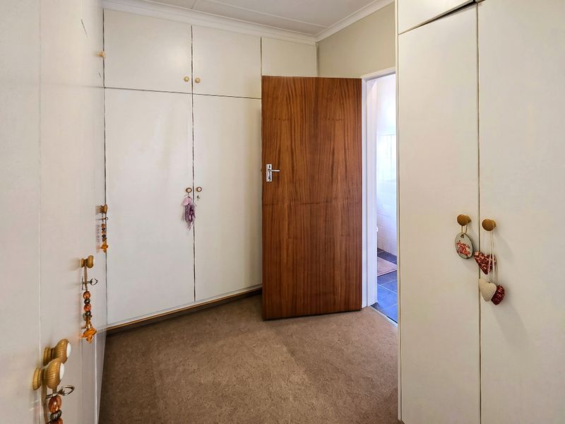 A bedroom featuring extensive built-in white cabinetry, carpeted flooring, and a wooden door leading to an adjacent room.