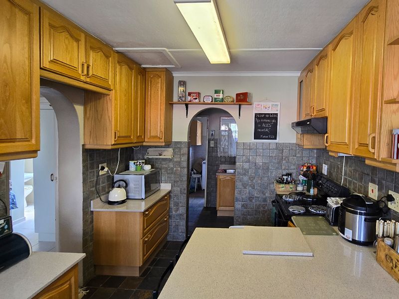 A functional kitchen featuring traditional wooden cabinetry, stone countertops, and a tiled backsplash, with an open archway leading to adjacent utility areas.