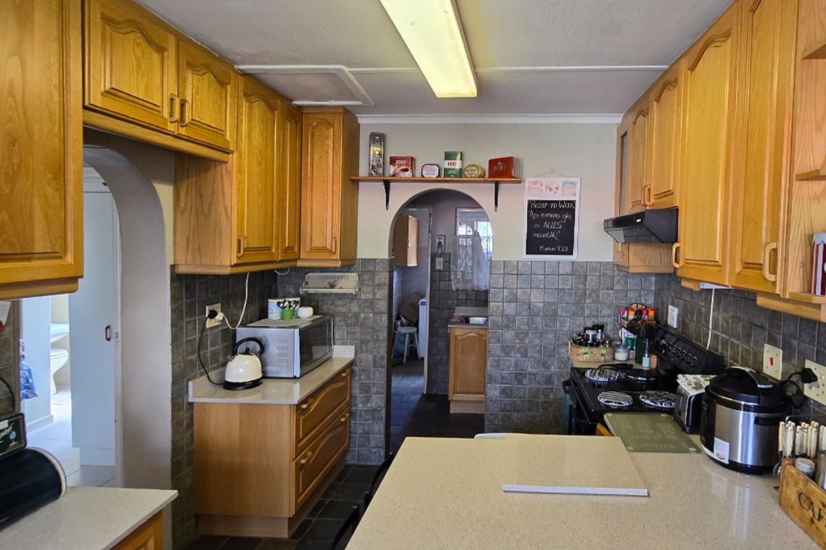 A functional kitchen featuring traditional wooden cabinetry, stone countertops, and a tiled backsplash, with an open archway leading to adjacent utility areas.