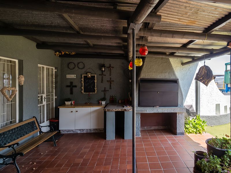Covered patio area featuring a built-in braai, tiled flooring, and timber roof structure, providing a functional outdoor entertainment space.