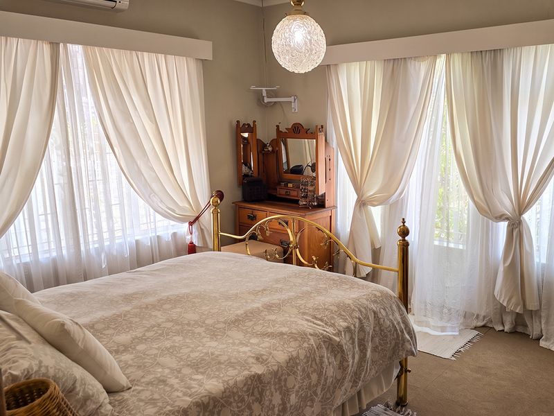 A well-lit bedroom featuring neutral walls, carpeted flooring, and large windows with curtain rails, providing a comfortable and functional living space.
