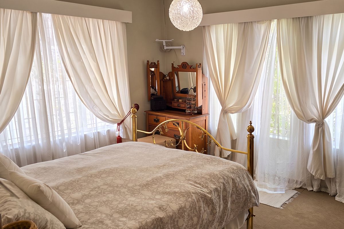A well-lit bedroom featuring neutral walls, carpeted flooring, and large windows with curtain rails, providing a comfortable and functional living space.