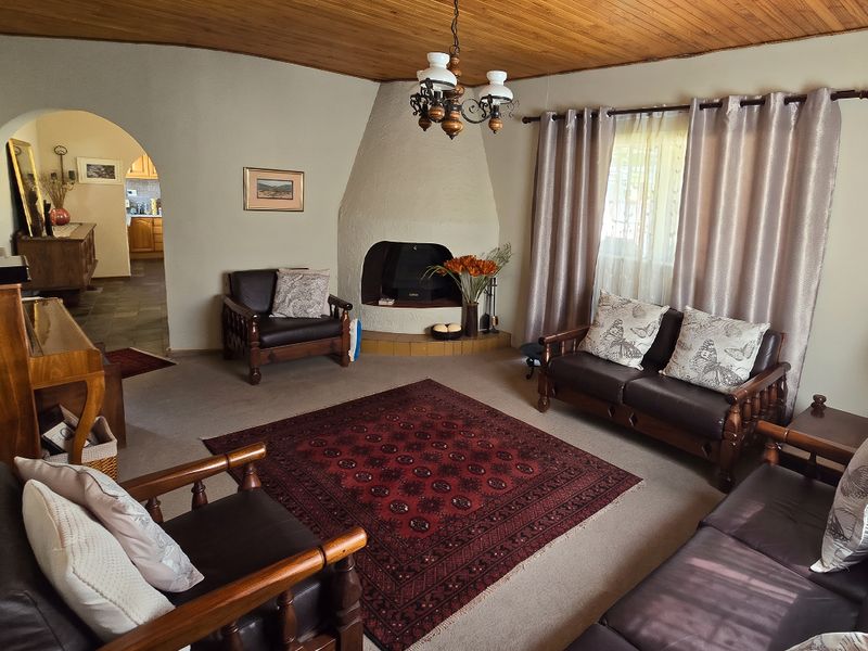 A cozy living room featuring a unique built-in fireplace, warm timber ceiling, and an arched entryway leading to the kitchen area.