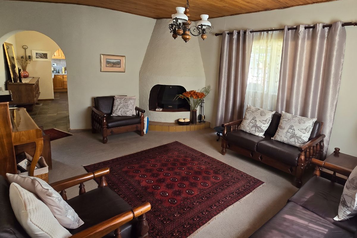 A cozy living room featuring a unique built-in fireplace, warm timber ceiling, and an arched entryway leading to the kitchen area.