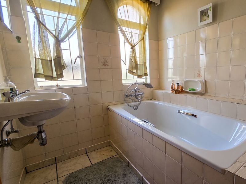 A functional bathroom featuring a built-in bathtub, pedestal basin, and neutral ceramic tiling throughout.