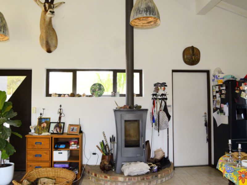 Living area featuring a central freestanding fireplace on a brick hearth, high ceilings with exposed beams, and a horizontal window providing natural light.