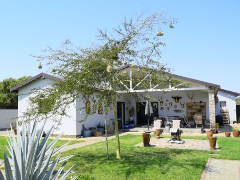 Rear view of the property featuring a covered patio with exposed roof trusses, brick detailing, and a well-maintained garden with paved pathways.