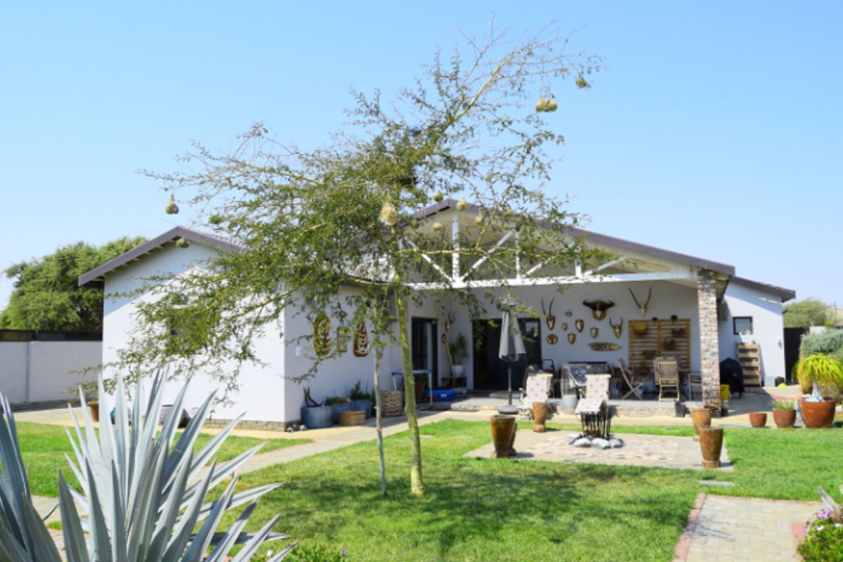 Rear view of the property featuring a covered patio with exposed roof trusses, brick detailing, and a well-maintained garden with paved pathways.