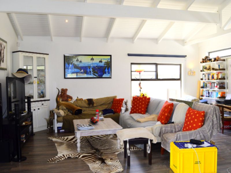 A spacious living room featuring exposed white-painted timber beams, laminate flooring, and large windows allowing for ample natural light.