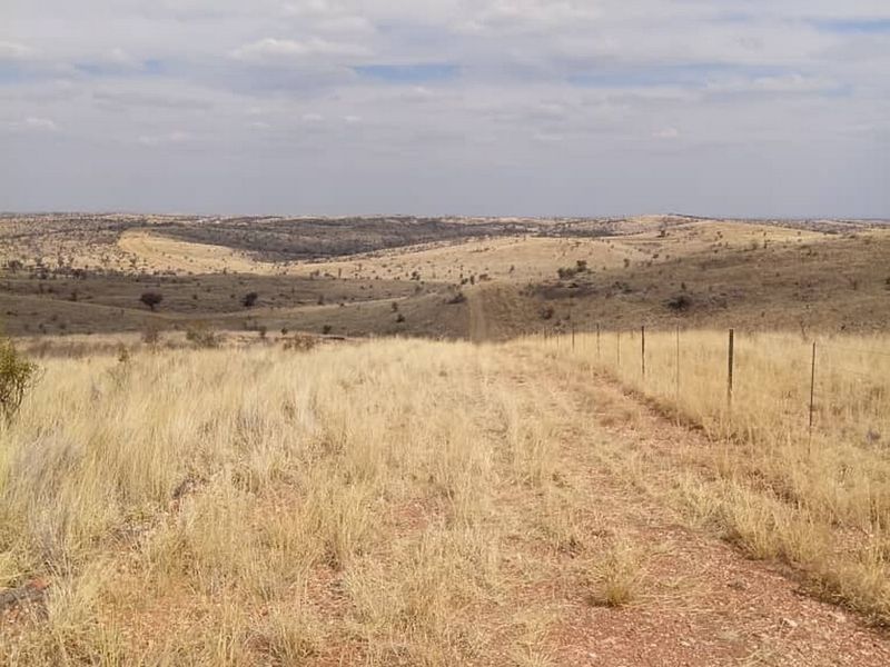 Expansive view of open, undeveloped residential land featuring natural dry grass terrain and a perimeter wire fence.