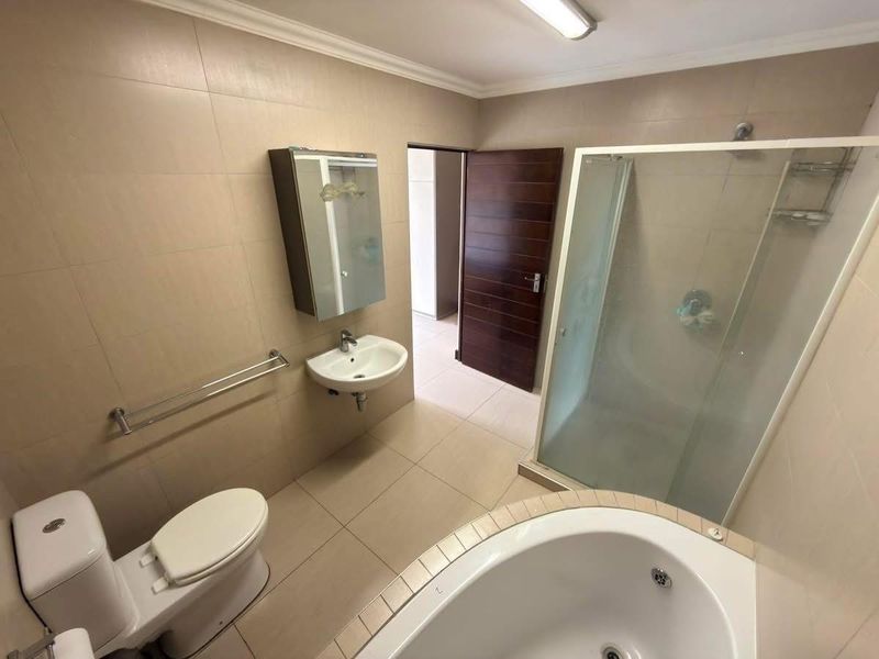 A clean, functional bathroom featuring a corner bathtub, separate shower enclosure, wall-mounted basin, and neutral floor-to-ceiling tiling.