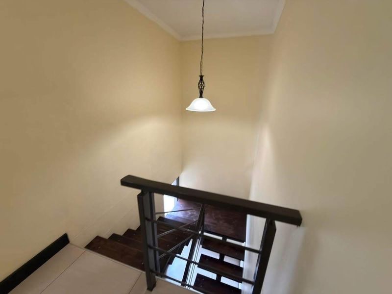 A view looking down a staircase featuring a wooden handrail, metal balustrade, and a pendant light fixture.