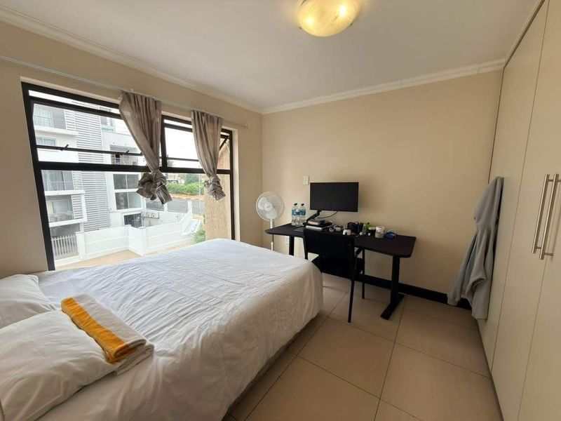 A functional bedroom featuring tiled flooring, built-in cupboards, and a large window providing natural light and an urban view.